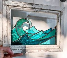 a person is holding up a stained glass piece in front of a white wooden frame