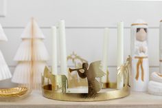 a gold candle holder with angel figurines and candles in front of christmas trees