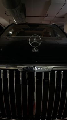 the front end of a black mercedes car in a garage with its hood up and lights on