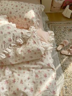 an unmade bed with pink and white flowers on it, next to a pair of slippers