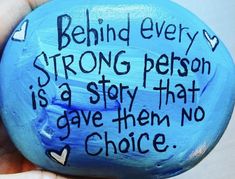 a hand holding a painted rock that says behind every strong person is a story that gave them no choice