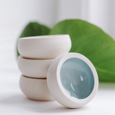 a stack of white bowls sitting on top of a table next to a green leaf