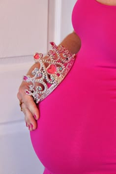 a pregnant woman in a pink dress with a tiara on her hand and belly