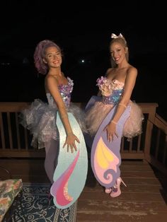 two girls dressed up as mermaids standing on a deck with their arms around each other