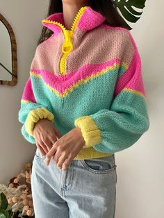 a woman standing in front of a mirror wearing a colorful sweater and jeans with yellow buttons