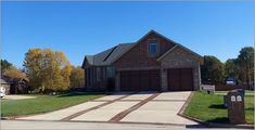 a large brick house sitting on top of a lush green field next to a driveway