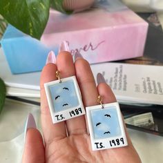 two square earrings with birds on them are shown in front of a stack of books