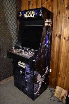 a star wars pinball machine sitting in front of a wooden paneled wall and fence