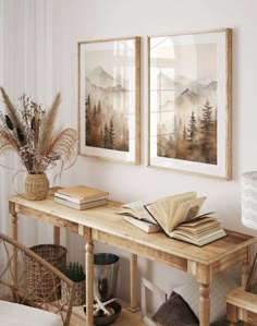 two framed pictures hang on the wall above a wooden table with books, plants and other items