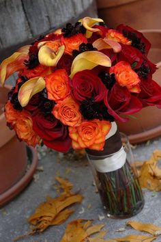 a bouquet of red and orange flowers in a vase on the ground next to potted plants