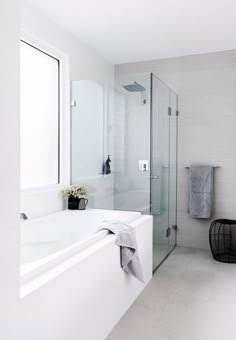 a white bathroom with a glass shower door and tub in the corner, next to a black trash can