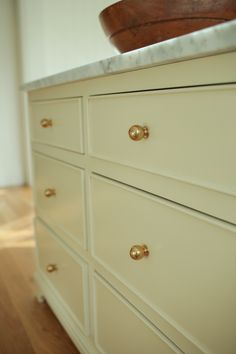 a white dresser with gold knobs on it's drawers and a wooden bowl on top