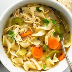 a white bowl filled with chicken noodle soup next to a piece of bread on a table