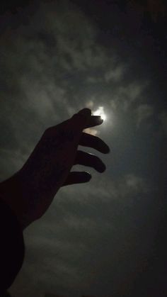 a person's hand reaching up into the sky at night with the moon in the background