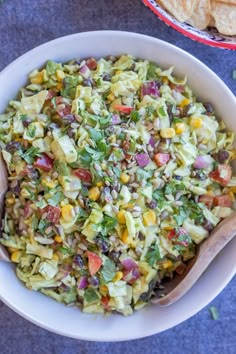 a white bowl filled with salad next to some tortilla chips on a blue surface