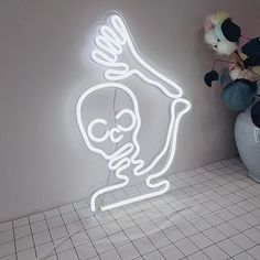 a neon sign with a skeleton on it next to a potted plant and stuffed animals