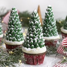 three cupcakes with frosted trees on them sitting on a plate next to christmas decorations