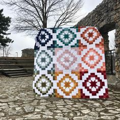 a colorful quilt is on display in front of a stone building