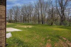 an empty yard with trees and grass in the back ground, next to a brick building