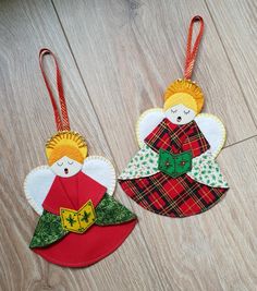 two christmas angel ornaments hanging from strings on a wooden floor, one is red and the other is green