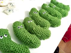 green crocheted cookies with eyes on them sitting on a white table next to other items