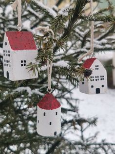 three ornaments hanging from a pine tree in the snow with red roofs and white houses on them