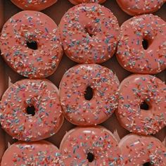 there are many donuts with pink frosting and sprinkles in the box