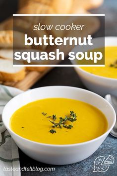 two bowls filled with butternut squash soup on top of a table next to bread