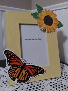 an orange and black butterfly sitting on top of a wooden frame next to a sunflower