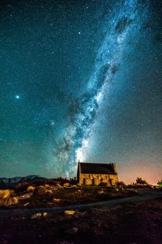 the night sky is filled with stars above an old church and mountain range in the distance