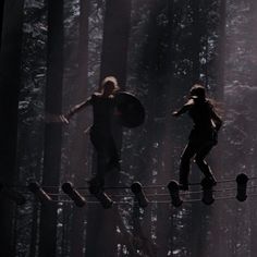 two people walking across a rope in the woods