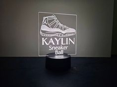 a lamp that is sitting on top of a table next to a black surface with the words kaylin sneaker ball in it