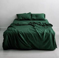 a bed with green sheets and pillows in a white walled room next to a wall