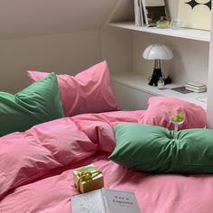 a bed with pink sheets and green pillows next to a book on top of it