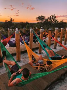 several people laying in hammocks on a dock at sunset or sunrise, while the sun is setting