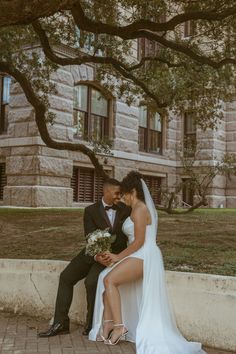 a bride and groom sitting on a bench under a tree