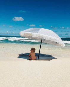 a baby sitting under an umbrella on the beach