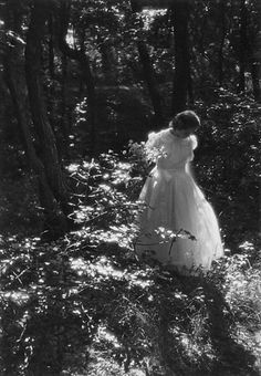 an old photo of a woman in a dress walking through the woods with her back to the camera