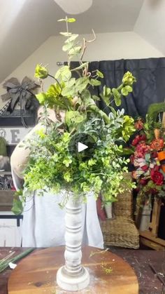 a vase filled with lots of green plants on top of a wooden table in a room