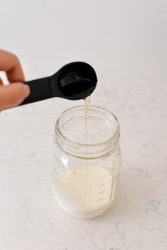 someone is pouring sugar into a jar with a measuring spoon on the side and another hand holding a black object in front of it