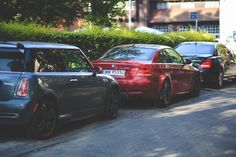 several cars parked on the side of a street next to trees and bushes in front of a building