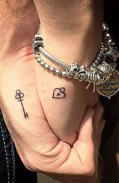 two people holding hands with tattoos on their fingers and one has a key to each other