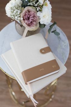 a white and brown notebook sitting on top of a table next to a vase with flowers