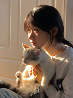 a woman holding a cat in her arms while sitting on the floor next to a door