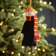 a christmas ornament with a doll hanging from it's side in front of a christmas tree