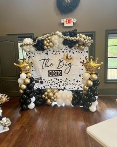 the big one balloon arch is decorated with black and white balloons, gold crowns, and confetti