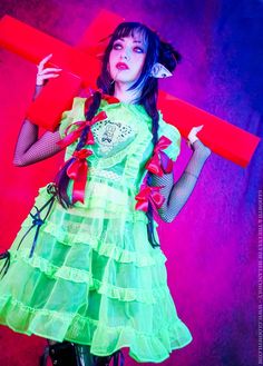 Neon green sheer dress worn in a gothic outfit by a model with long braided hair holding a red neon cross.