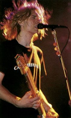 a man with long hair holding a guitar in front of a microphone