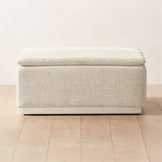 a white ottoman sitting on top of a hard wood floor next to a planter