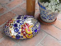 a colorful rock sitting on top of a brick floor next to a potted plant